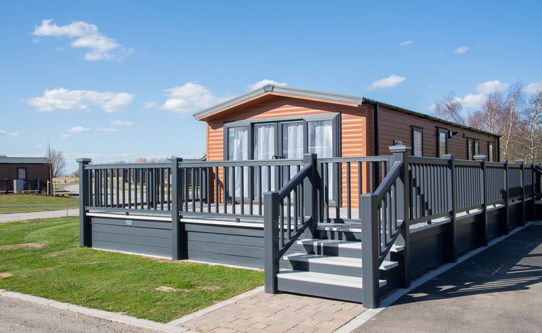 A photo of a wooden holiday lodge at our holiday park Appletree, Lincolnshire on a cloudy sunny day.