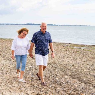 A mature hetero white couple are walking along the sands of Mersea Island beach, Essex.