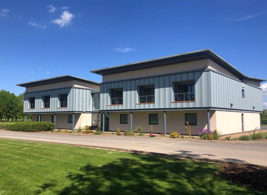 A big blue sky and green grass frame the image that features a two story hotel building.