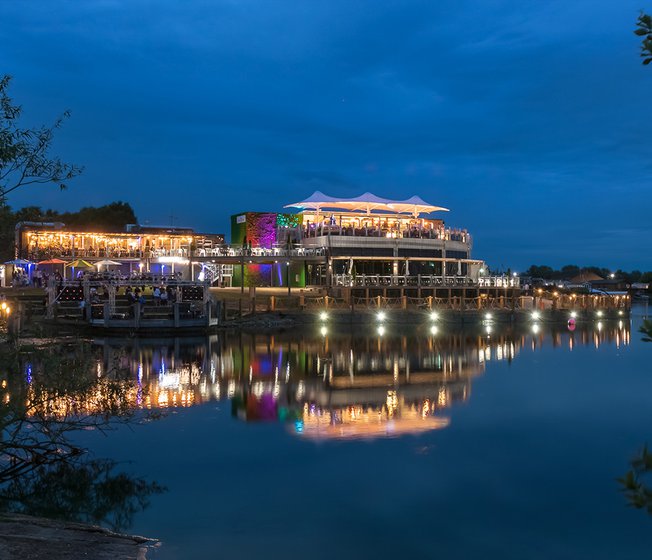 Our Tattershall Lakes holiday park. There is an evening view of the holiday park, with the lights shining bright, and many evening activities taking place in the park.